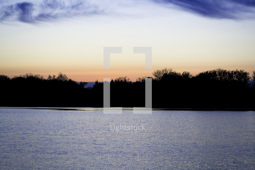 Silhouette of a treeline with sunset over a lake.