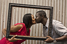 Couple kissing behind empty picture frame