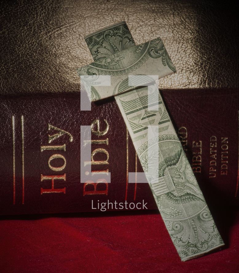 Dollar bill cross leaning against a Bible.
