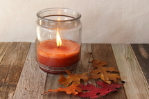 flame on a fall candle and fall leaves on wood 