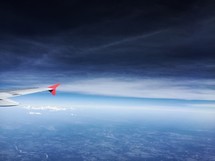 wing of a plane flying under storm clouds 