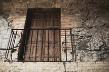 Iron balcony with wooden doors on a brick wall