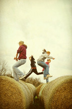 Children jumping across barrels of hay.