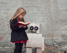 a girl reading a book to a robot 