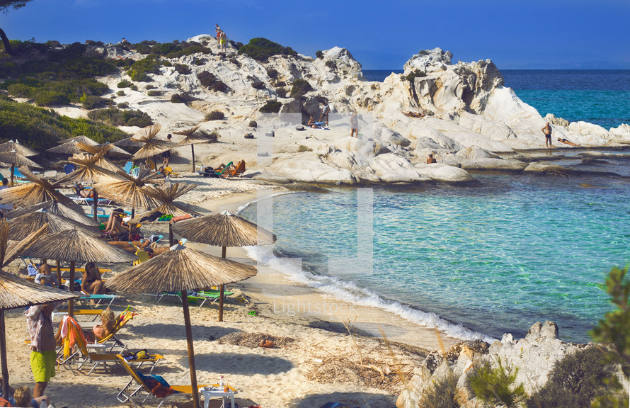 Aegean sea coast with greenery around, rocks and bushes, blue water with waves, Greece