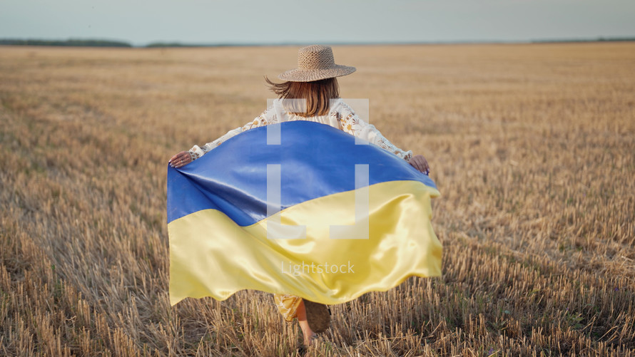 Ukrainian patriot woman running with national flag in wheat field. Beautiful girl in embroidered ethnic traditional shirt. Ukraine, independence, democracy, victory in war.