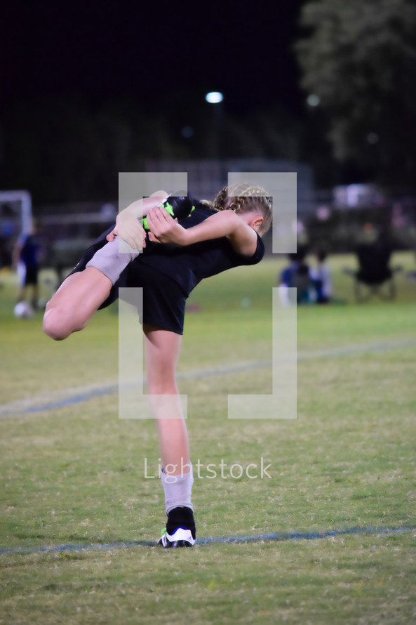 a girl soccer player stretching on the soccer field 