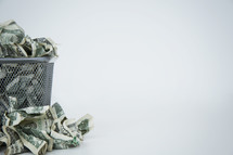 crumpled dollar bills in a trash can 
