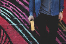 A young man standing in front of a geometric pattern on a wall holding a Bible 