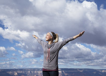 a woman standing at the top of a canyon with open arms 