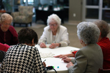 Seniors playing dominoes at a round table.
