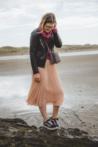 a woman in a skirt and sneakers walking on a beach 