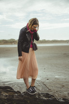 a woman walking on a beach in a skirt and sneakers 