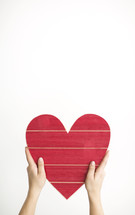hands holding up a red wooden Valentine's Day heart 