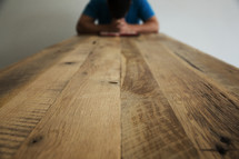 man praying over a Bible at the end of a table 
