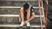 young man sitting on steps tying his shoes 