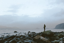 a man standing on a rocky shore in winter 