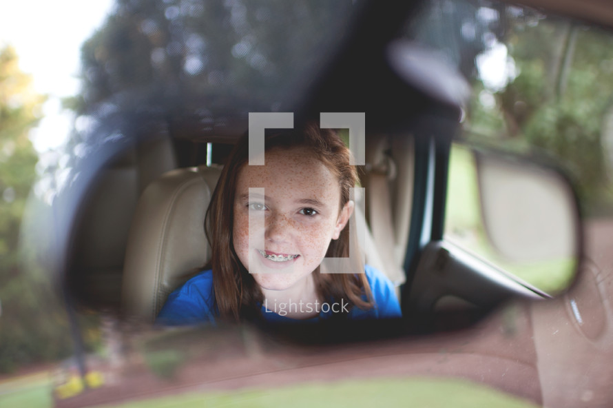 smiling face of a girl child in a rearview mirror 