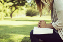 a woman sitting on a park bench in prayer