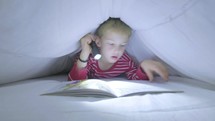 Boy reading a book by torch under the bed