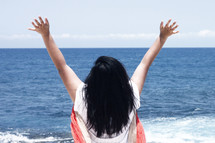 a woman standing on a beach with hands raised 
