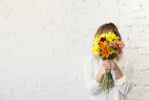a woman holding a bouquet of flowers and hiding behind them 
