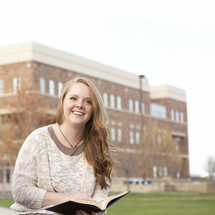 a young woman on a college campus reading a book 