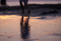 reflection in water of a boy walking on a beach 
