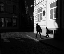 shadow of a man walking on a sidewalk beside of a cobble stone street 
