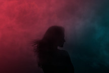 silhouette of a woman against a smoky pink and blue background 
