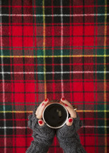 woman in gloves holding a mug over red plaid background 
