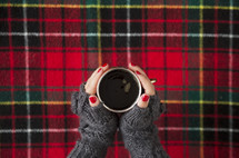 a woman in gloves holding a mug over red plaid background 