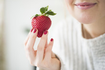 a woman holding a red strawberry 