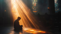 Sunlit prayer. Young man praying in the church in the sunbeams shining through the window.