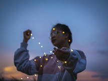 a young woman holding a string of fairy lights 