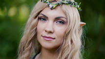 Portrait of young woman in cosplay elf clothes with make-up on green background. Fantastic look, long blonde hair, forest crown. Halloween concept. High quality photo