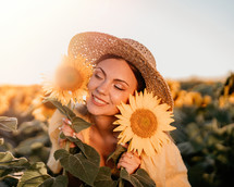 Beautiful young woman in straw hat posing with sunflowers. Blooming field. Happy smiling girl. Trendy outfit, vintage retro style