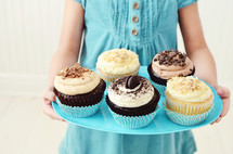 a girl child holding a plate of cupcakes 