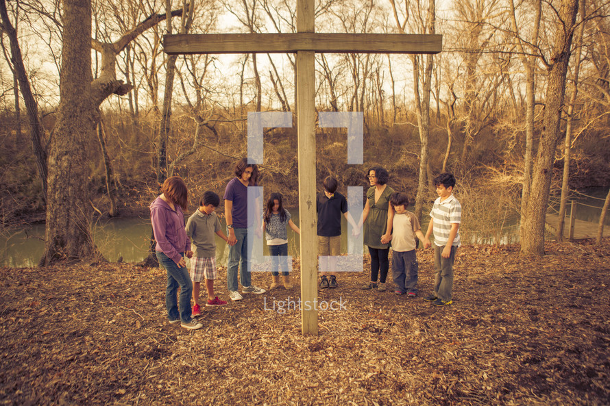 holding hands in prayer standing around a cross 