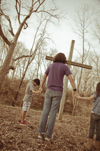 Mother and children holding hands before a wooden cross.