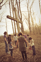 holding hands in prayer around a cross outdoors 