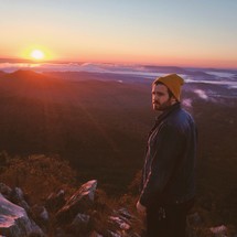 man standing at the top of a mountain under sunlight