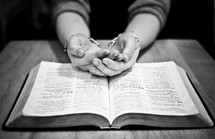 hands cupped in prayer over a Bible
