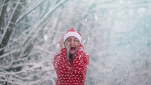 Cheerful woman enjoys winter wonderland. Snow flies on her and she is happy, rejoices cold weather. Girl in red Christmas sweater and Santa hat. High quality photo