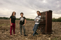 teens standing next to an old piano in a field 