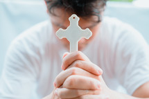 a man holding a cross praying with head bowed 