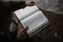 Little boy reading the Bible at a table.