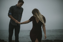 a couple walking on a rocky shore holding hands 