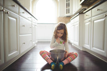 girl in pajamas a kitchen licking a bowl
