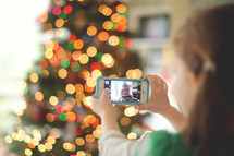 child taking a picture with a cellphone of a Christmas tree 